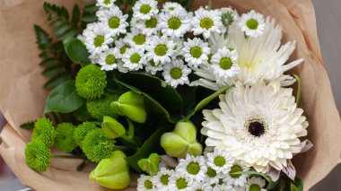 Sarılı yeşil ve beyaz çiçekler, el işi kağıdına sarılı buket..