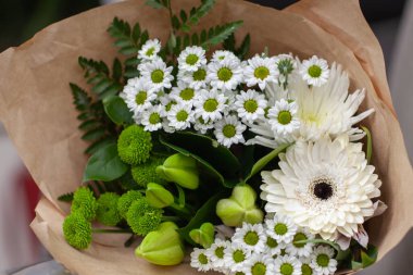 Sarılı yeşil ve beyaz çiçekler, el işi kağıdına sarılı buket..