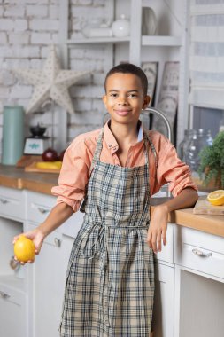 Evdeki mutfakta taze limon pişiren zenci çocuk. Afrikalı çocuk hazırlanıyor. Sağlıklı salata hazırlığı. Çiğ malzemeler masada. Aile iletişimi, aşçılık ve hafta sonu tatili.