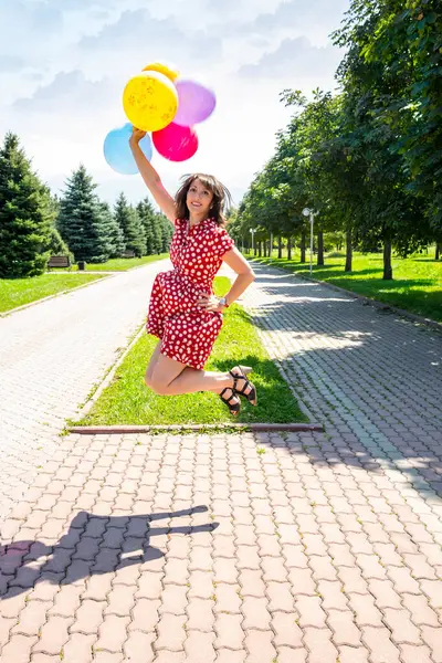 Happy woman jumping with colored balloons outdoors in the park