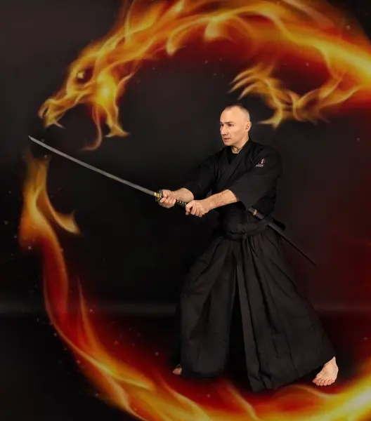 Portrait of aikido sensei master with black sensei belt in taekwondo kimono witn sword katana on black background. Traditional samurai hakama kimono. Healthy lifestyle and sports concept.