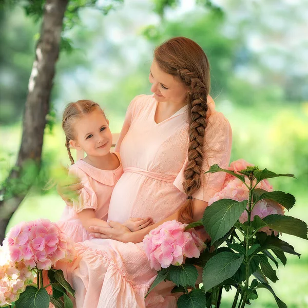 Güneşli bir yaz gününde, kızıyla birlikte gülümseyen mutlu anne. Anne ve kız çocuğu, çiçek açan güzel bir bahçede, gartensiya çiçekleriyle. Mutlu aile