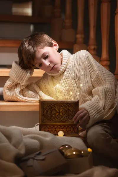クリスマスの階段の近くに素晴らしい箱と贈り物を持って座っている少年 新しい年 幸せと妖精の物語 ロイヤリティフリーのストック画像