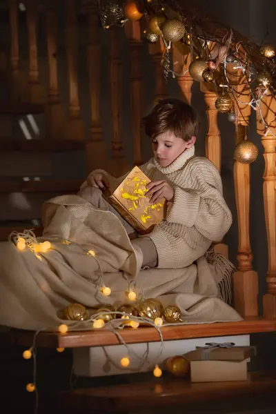 クリスマスの階段の近くに素晴らしい箱と贈り物を持って座っている少年 新しい年 幸せと妖精の物語 ストック画像