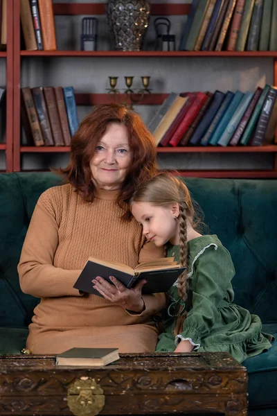 ハッピーおばあちゃんと孫娘が一緒に本を読んで 自宅で楽しんでいる ストックフォト