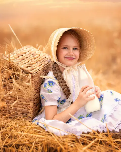 日落时一个快乐的女孩在麦田里的画像 一个小孩拿着一个装有牛奶的玻璃瓶 放在黑麦耳朵的背景上 具有野餐性质 免版税图库照片