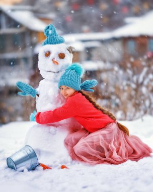 Çocuk buz gibi kışın kardan adam yapar. Çocuk havuçtan burun yapıyor. Yeni yılın kışında Noel tatilinde açık hava aile eğlencesi