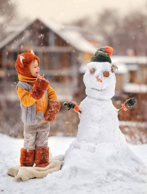 Yeni yıl kedi kostümü giymiş küçük çocuk kışın soğuk bir günde kardan adam yapar. Çocuk havuçtan burun yapıyor. Yeni yılın kışında Noel tatilinde açık hava aile eğlencesi