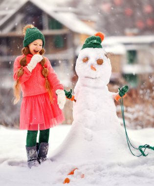 Çocuk buz gibi kışın kardan adam yapar. Çocuk havuçtan burun yapıyor. Yeni yılın kışında Noel tatilinde açık hava aile eğlencesi