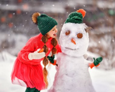 Çocuk buz gibi kışın kardan adam yapar. Çocuk havuçtan burun yapıyor. Yeni yılın kışında Noel tatilinde açık hava aile eğlencesi