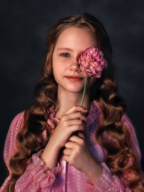 Pembe elbiseli, esmer arka planda şakayık çiçekli güzel bir kız. Romantik, neşeli bir görüntü.