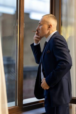 Sigara içerken camında sigara olan takım elbiseli yakışıklı bir iş adamı.