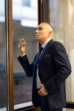Sigara içerken camında sigara olan takım elbiseli yakışıklı bir iş adamı.