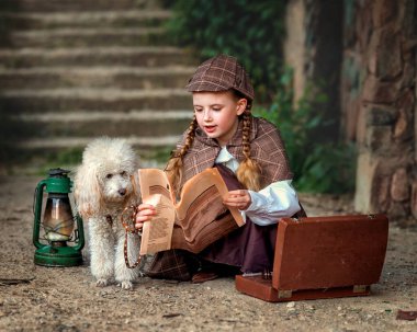 A girl child in a detective costume with a poodle dog investigates in autumn garden. The photo has a cinematic, old-fashioned atmosphere