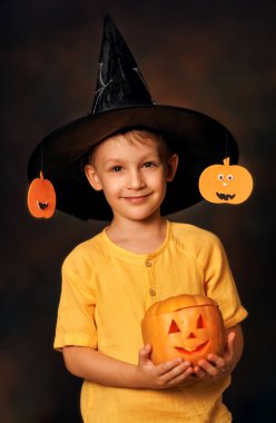 Charming autumn portrait of smiling boy kid holding carved pumpkin in Halloween