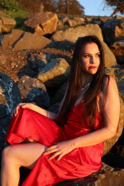 Kırmızı elbiseli, kayaların üzerinde oturan güzel beyaz bir kadının fotoğrafı. 