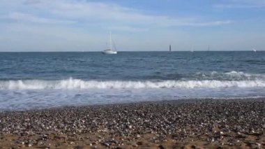 Deniz kıyısında sakin bir deniz manzarası ve arka planda yatlar. Akdeniz Barselona İspanya 'sının çakıl taşlı sahilinde kıyı dalgaları. Deniz manzaralı Barceloneta 'daki ünlü Sant Miquel plajında kimse yok.