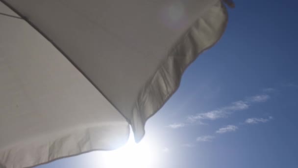 夏日的晴空万里 白沙滩上的雨伞在微风中飘扬 从海滩下的遮阳伞下的天空背景和复制空间观看 防止夏季海滩过热 — 图库视频影像