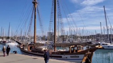 İnsanlar deniz kenarındaki ünlü gezinti yolu boyunca yürüyorlar. Lüks yatları ve eski ahşap yelkenlisi olan Panning Bay. Deniz manzaralı Moll de la Fusta, Bosch i Alsina. Barselona, İspanya 05 11 2021