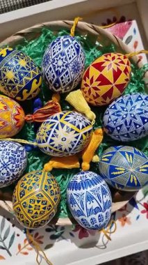 Paskalya yumurtaları geleneksel Ukrayna pysanky tekniklerini sergiliyor, karmaşık halk modelleri sergiliyorlar. Paskalya kutlaması için dekoratif bir sepete güzelce yerleştirilmiş..