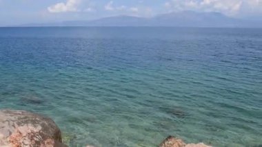 Agii Apostoli 'nin karşı kıyısından Euboea adası manzarası sakin mavi suları gösteriyor. Manzara, Evia 'nın kayalık kıyıları ve uzak dağlarının birleşiminden oluşuyor ve sakin bir atmosfer yaratıyor.