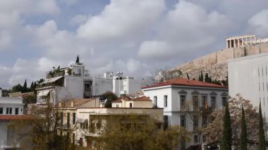 Atina 'daki tarihi Akropolis çevresindeki çatılara bakan büyüleyici Yunanistan manzarası. Geleneksel binaların ve açık mavi gökyüzünün altındaki canlı Yunan manzarasının güzelliğini hissedin..