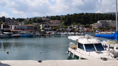Yunanistan 'daki Saint Apostles köyünün sakin marina iskelesi tekne ve ziyaretçilerle dolup taşıyor. Yeşil tepelere yaslanmış sahil manzaralı restoran ve binalar kıyı atmosferi yaratıyor..