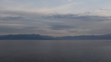 Serene Vista, sakin suları ve alacakaranlığın yumuşak gölgelerini gökyüzünde sergiliyor ve çarpıcı yansımalar yaratıyor. Uzak dağlar ufuk çizgisinde, barışçıl atmosfere katkı sağlıyor..