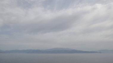 Uçsuz bucaksız sakin sular yumuşak bulut örtüsünü yansıtırken uzak dağlar barışçıl bir zemin sağlar. Sabahın erken saatlerinde bu sahil bölgesindeki olay yerinin sakinliğini arttırır..