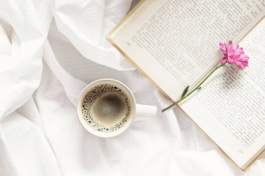 Sabah havasında, bir fincan aromatik kahve, güzel bir çiçek ve yatakta ilginç bir kitap.