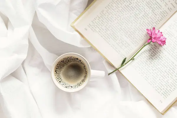 Sabah havasında, bir fincan aromatik kahve, güzel bir çiçek ve yatakta ilginç bir kitap.