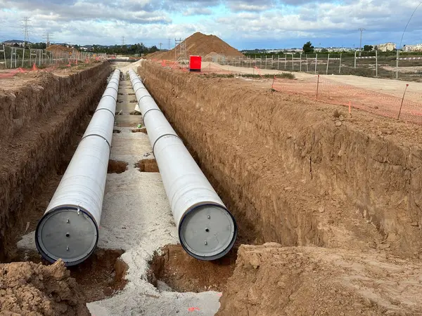 Large industrial pipes laid in a deep trench for infrastructure development against a cloudy sky
