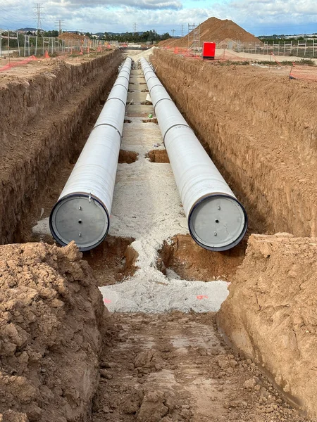 Large industrial pipes laid in a deep trench for infrastructure development against a cloudy sky