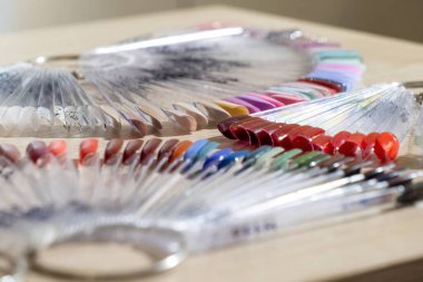 Tahta masanın üzerinde metal halkalar olan çivi örnekleri. Vantilatör şekilli plastik paletler, manikür salonundaki tanıtım için son derece yakın çekim ipuçları.