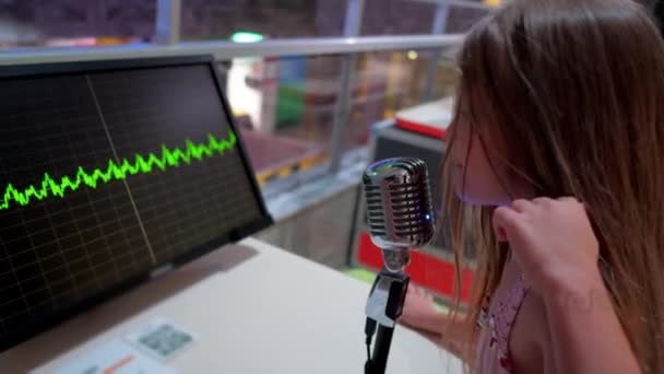 活泼的女孩在感情上唱歌 对着话筒尖叫 小女生在模糊的背景特写中看着监视器上移动的声波 — 图库视频影像