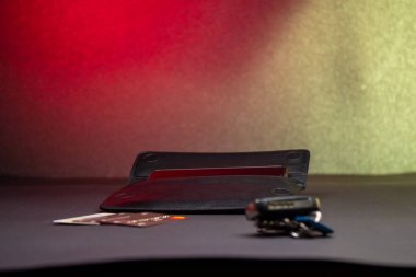 Erkekler için siyah uzun deri cüzdan gri yüzeyde kredi kartları ve anahtarların yanında açık duruyor. Kırmızı ve sarı gradyan arka planda moda aksesuarları