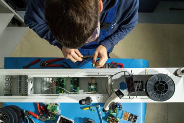 Mühendis anakart ve lehim kablolarıyla çalışıyor. Teknisyen daha iyi çalışmak için araçlar kullanır ve şarj prizine yükleme yapmaya çalışır