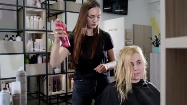 Długowłosy Stylistka Posypuje Włosy Młodej Blondynki Lakierem Włosów Profesjonalny Fryzjer — Wideo stockowe