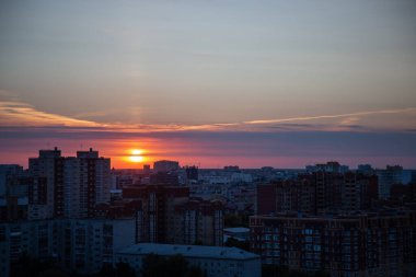 Turuncu günbatımı, akşam kentinde yerleşim alanındaki binaların arkasında saklanır. Güneş ışığı, şehri aydınlatmak için son ışınları ve yaklaşan geceyle ilgili sinyalleri gönderir.