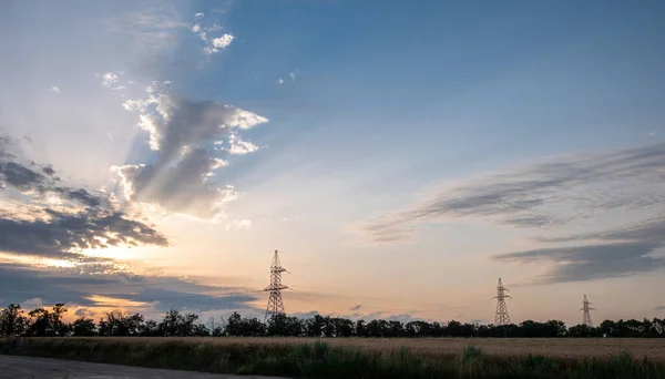 Power transmission lines transfer clean energy. Sunset illuminates countryside farmland with power substation towers transporting renewable energy