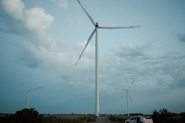 環境に優しい風車はきれいなエネルギーを生み出します 車で観光客は夜の青空に対して再生可能エネルギーを生成する風力タービンを探索します — ストック写真