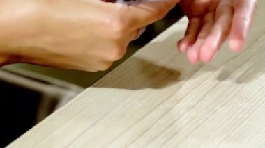 Genç müşterinin elleri, güzellik salonundaki tırnaklara renkli plastik uçlu jel cilasının rengini seçiyor. Ahşap masada manikür yapan kadın.