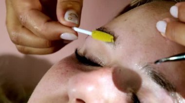 Modern güzellik salonunda kaş kaplama işlemi. Profesyonel sanatçının elleri saç tarama şeklini kozmetik fırçasıyla yakından tarar.