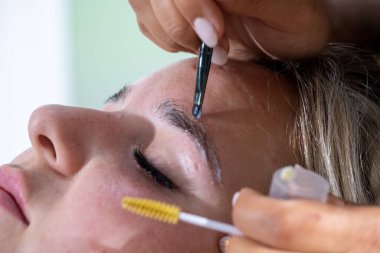 Makyaj sanatçısının elleri, kaşları fırçayla kaplamak anlamına gelir. Güzellik salonundaki kaşların profesyonelce kaplanması ve renklendirilmesi.