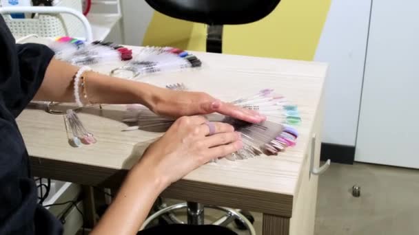 年轻的无名女子在塑料调色板上涂上彩色的指甲凝胶抛光漆样品 时尚的客人在美容室准备修指甲 — 图库视频影像