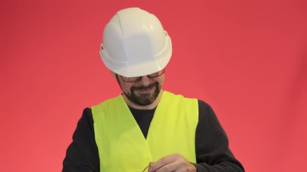 好奇心旺盛なエンジニアがプレゼントバッグに手を入れてくれます 髭を生やした男で白いハードハットの笑顔立っている赤の背景クローズアップスローモーション — ストック動画
