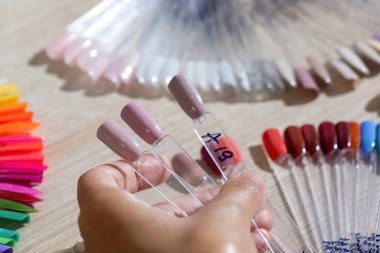 Kadın eli, tırnak jölesi renginde örnekler tutuyor. Güzellik salonunda manikür tasarımlarını sergilemek için hayran şekilli plastik uçlar.