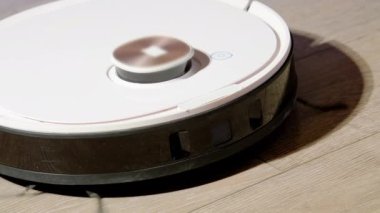 Robot süpürgesi yanıp sönen göstergeyle oturma odasının zeminini temizliyor. Çağdaş ev aletleri yakın görüntüde