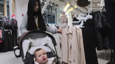 Bebek arabasında oğlu olan Müslüman bir kadın kıyafet reyonunda ceket arıyor. Şaşkın suratlı oğlum etrafa bakıyor ve alışveriş merkezini keşfediyor.