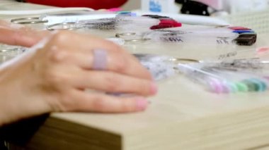 Tanımlanamayan müşteri tahta masada oturuyor ve manikür tırnak tasarımı örnekleriyle plastik çubukları hareket ettiriyor. Genç bir kadın güzellik salonunda oje rengini seçiyor.